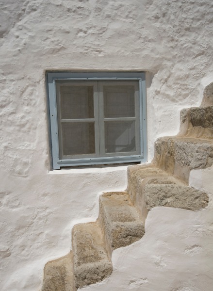 Weiß gekalkte Hauswand mit kleinem blauen Fenster und steinernen Stufen