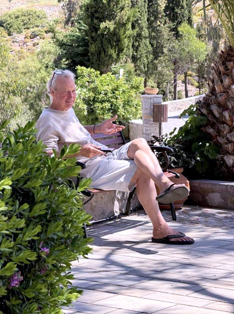 Paul Skorpen sitzt im Sonnenschein auf einer Bank zwischen grünen Pflanzen auf Patmos und erzählt