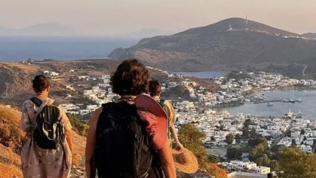 Eine kleine Gruppe wandert bei Sonnenuntergang über einen Hügel auf Patmos, unter ihnen Skala und das Meer